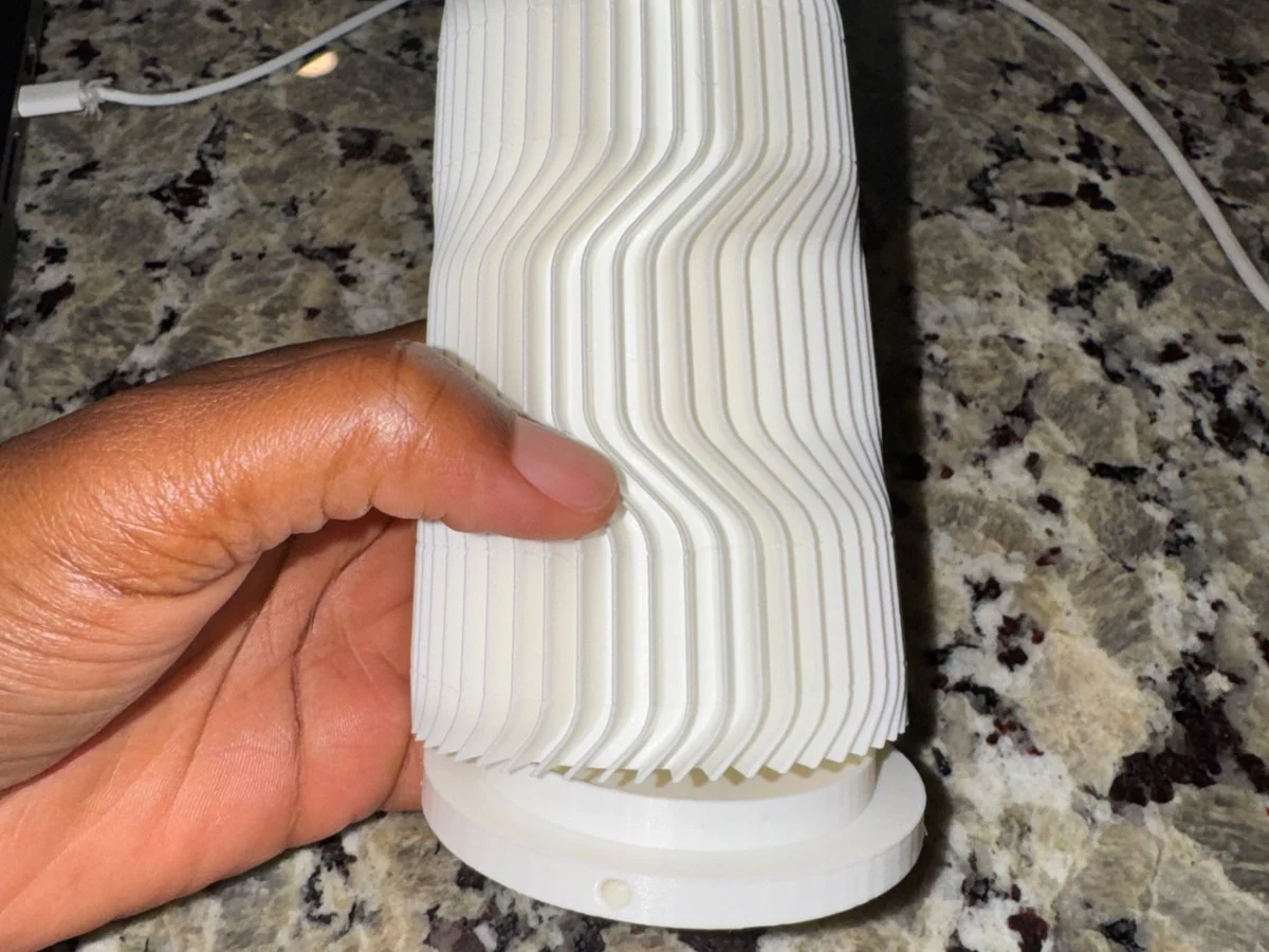 Hand holding the ribbed, 3D-printed FOCUS lamp enclosure seated on its white base