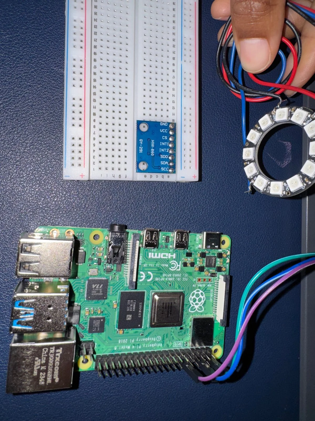 Raspberry Pi 4 wired to a NeoPixel LED ring, with a breadboard and sensor module on a desk